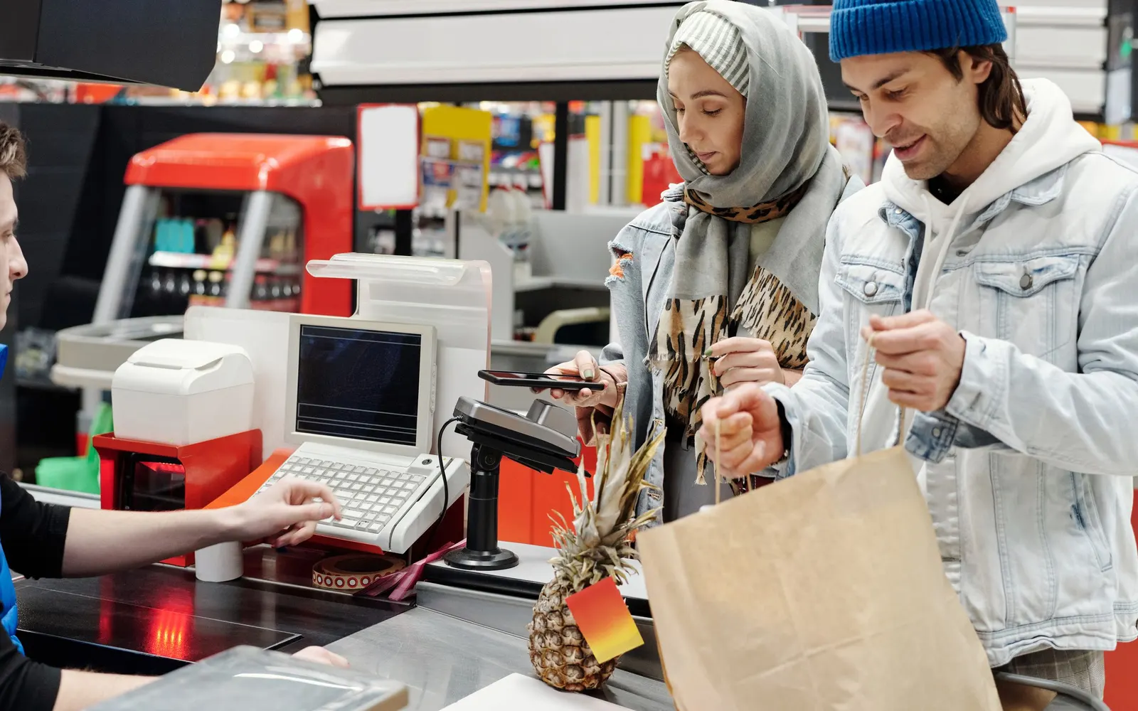 Ein Paar bezahlt an der Supermarktkasse und packt seinen Einkauf in eine Papiertüte