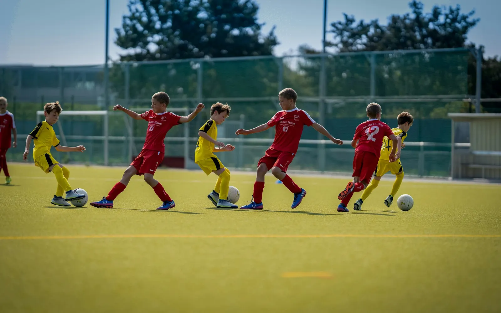 Kinder einer Jugendfußballmannschaft in roten und gelben Trikots spielen auf einem Kunstrasenplatz